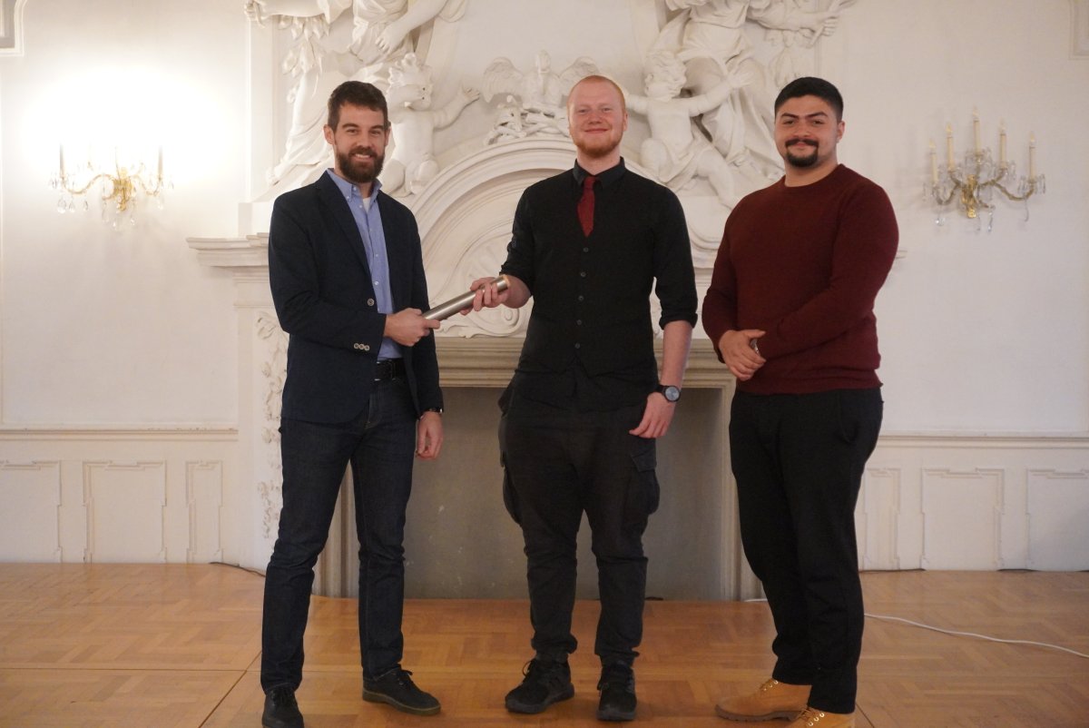 Das Bild zeigt, wie der SMV-Mitarbeiter des SG 42.1, Jens Kußmann, den Staffelstab an den neuen Bezirksschülersprecher John Reinhardt (Staatliche Berufsschule Lichtenfels) übergibt. Rechts im Bild ist der stellvertretende Bezirksschülersprecher Hartmut Krings (Staatliche Berufsschule Hof) zu sehen.